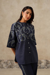 A woman modeling a navy blue short-sleeve kurta with a light blue paisley pattern and a button-down front, paired with matching navy pants, set against a textured beige wall.