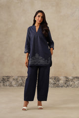 A woman modeling a denim coord set kurta set with matching wide-leg trousers, featuring a V-neckline and embroidered detailing near the hem, cutwork embroidery