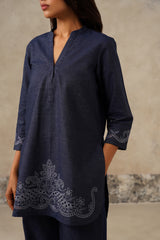 A woman wearing a navy blue denim tunic top with tonal embroidered paisley patterns on the hem and cuffs