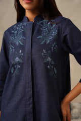 A close-up of a woman wearing a dark navy blue tunic top with light blue-green floral embroidery on the chest