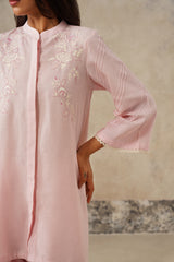 A close-up of a woman wearing a light pink kurta with delicate white floral embroidery on the chest and sleeves, featuring a mandarin collar and three-quarter bell sleeves with scalloped edges.
