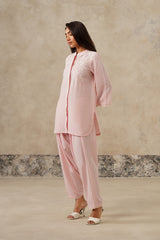 A woman models a light pink coord set outfit consisting of a long-sleeved embroidered kurta and matching dhoti style pants, floral embroidery